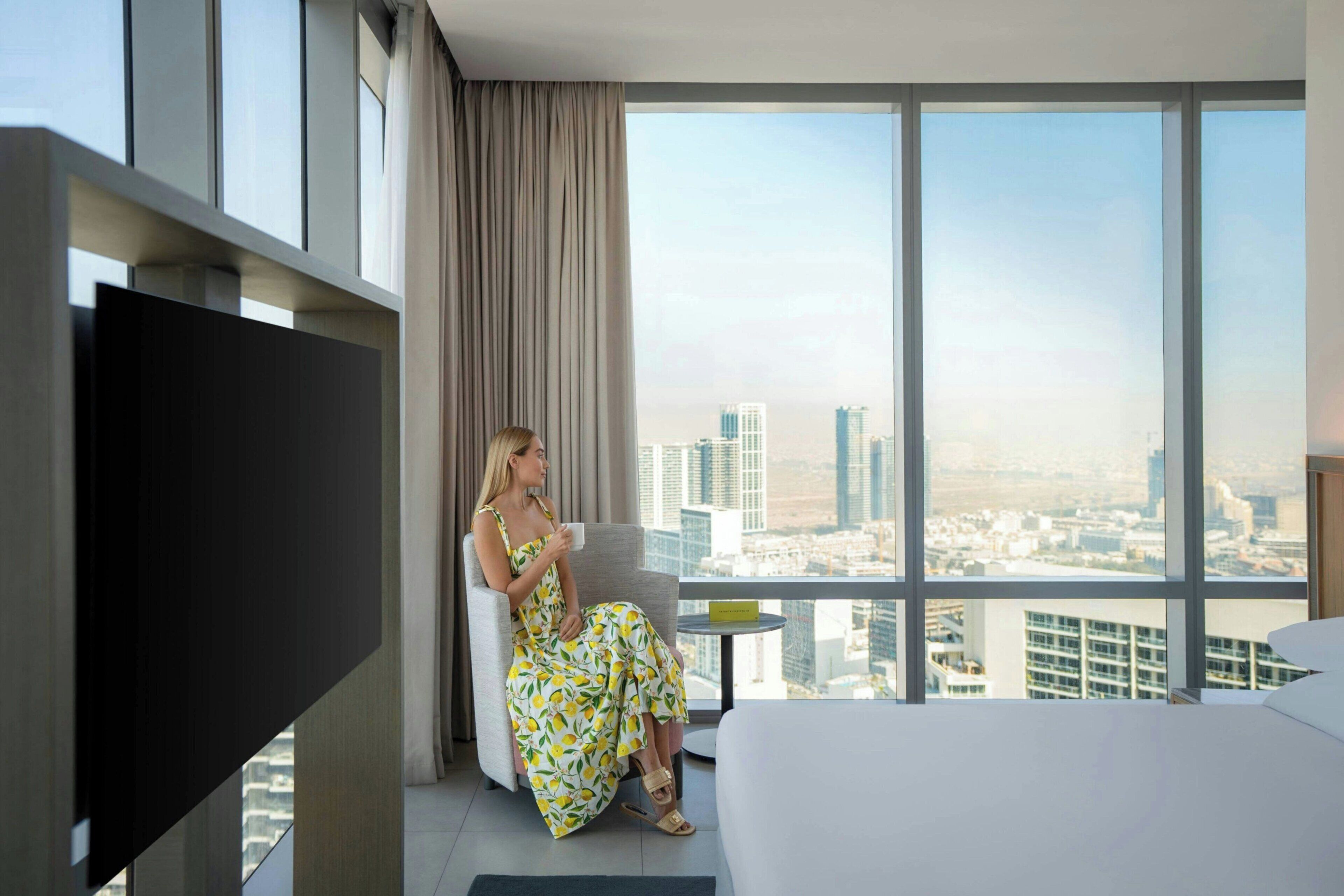 A hotel room with a large window, a bed, a TV, and a chair.
