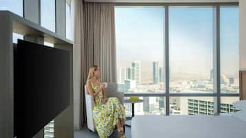 A hotel room with a large window, a bed, a TV, and a chair.