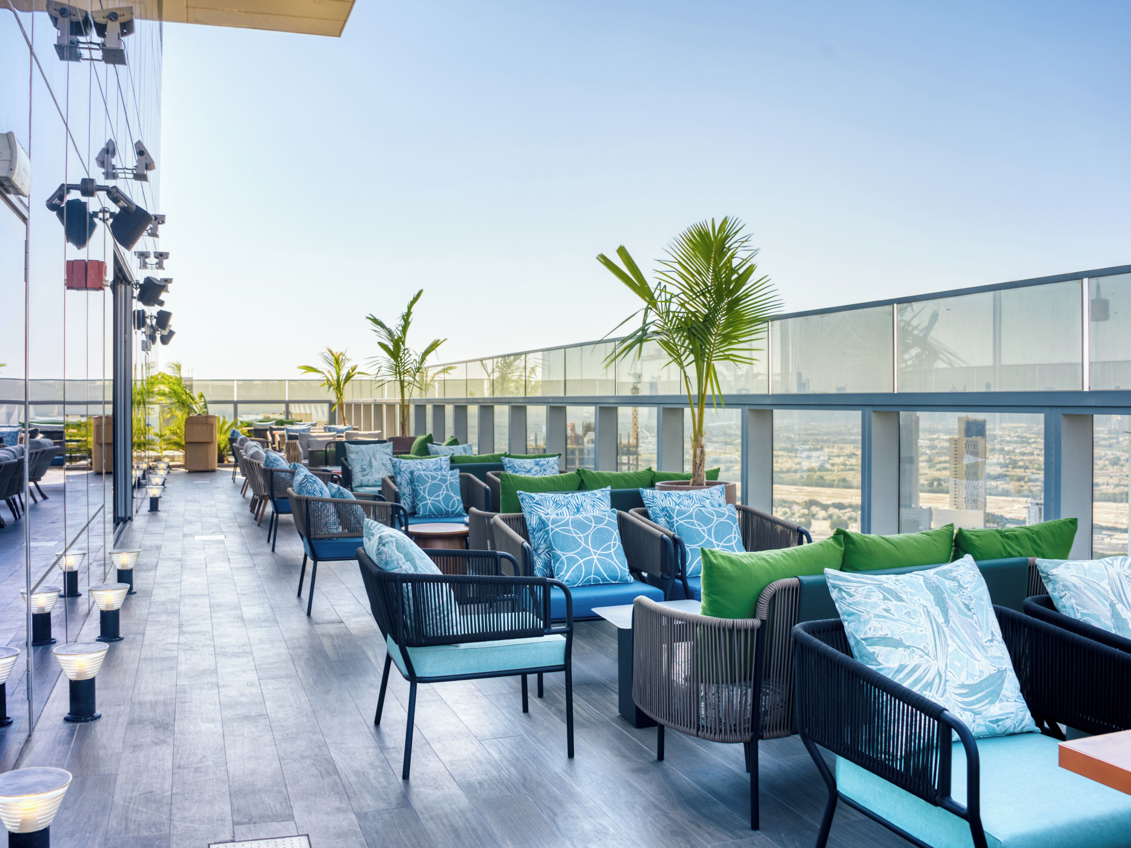 A rooftop bar with outdoor seating, including chairs and tables, and a view of the cityscape.