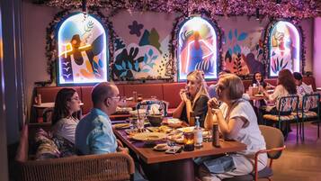 Un restaurante con cabinas y mesas, con un techo decorado con follaje colgante y obras de arte en las paredes.