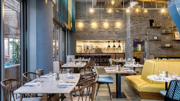 Un interior de restaurante moderno con paredes de ladrillo, lámparas colgantes y una mezcla de asientos de madera y tapizados.