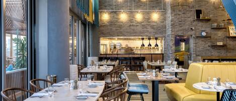 Un interior de restaurante moderno con paredes de ladrillo, lámparas colgantes y una mezcla de asientos de madera y tapizados.