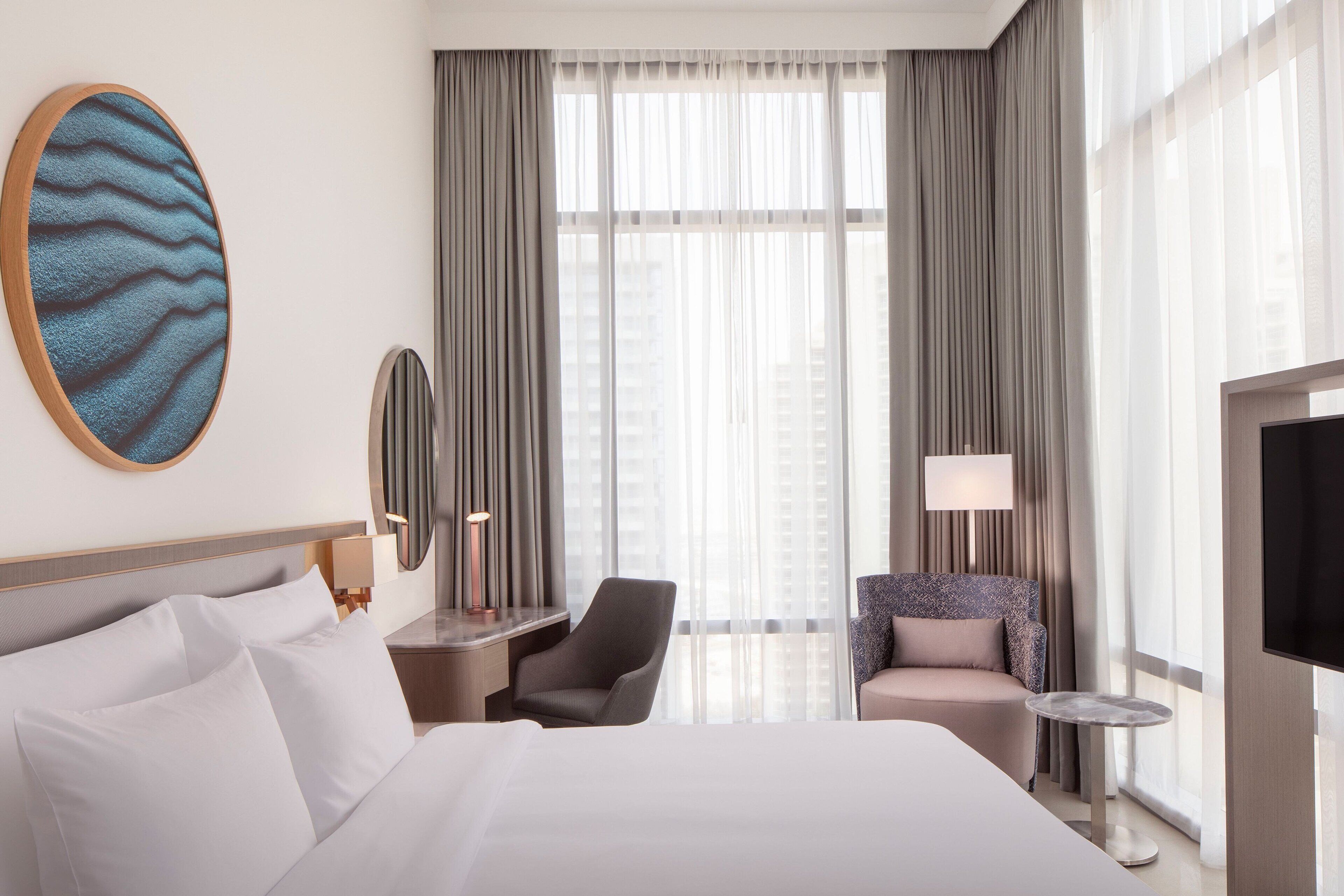 Ein Hotelzimmer mit einem großen Bett, einem Schreibtisch mit Lampe, einem Sessel und einem Fernseher.