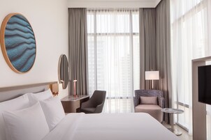 Una habitación de hotel con una cama grande, un escritorio con lámpara, una silla y un televisor.