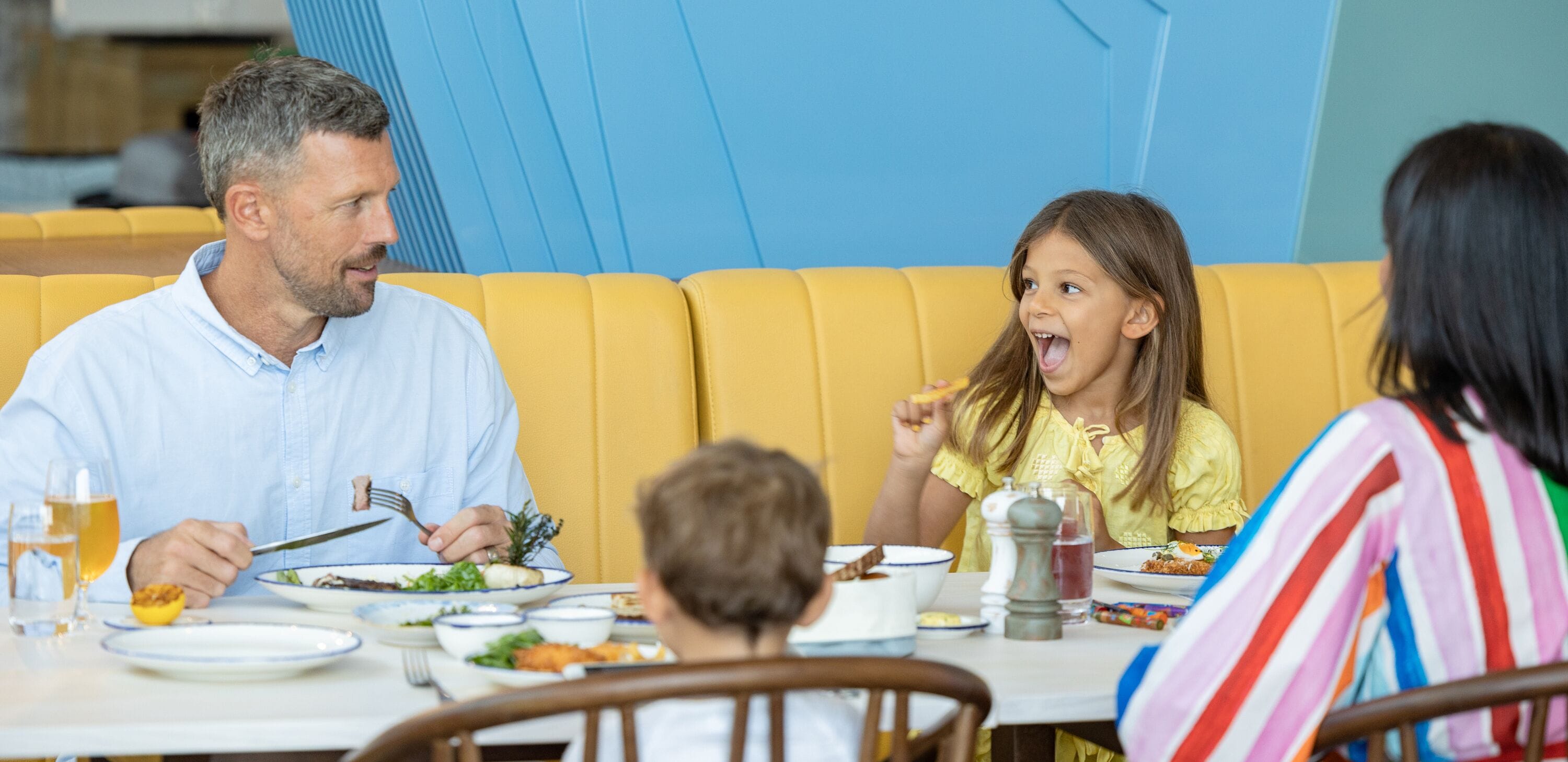 Una familia cenando en una mesa con asientos acolchados amarillos.
