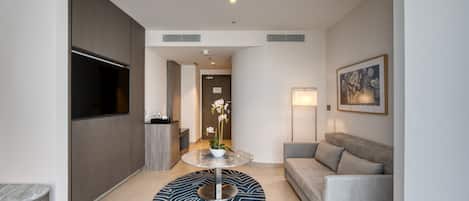 Una sala moderna con un sofá, una mesa redonda de centro con un arreglo floral, un televisor de pantalla plana montado en la pared y un cuadro abstracto enmarcado.