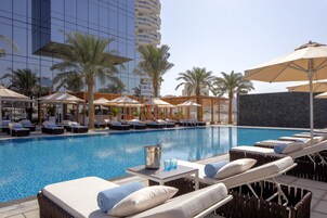 Un área de piscina de hotel con sillones, sombrillas y una piscina azul cristalina.