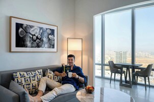 A person reading a book on a couch with a city view, a table with chairs, and a bowl of fruit on a table.