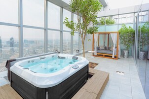 A modern indoor relaxation area with a hot tub, a seating area with a canopy, and a view of a cityscape through large windows.