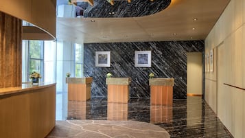 A modern lobby with marble floors, wooden reception desk, and framed artwork on the walls.