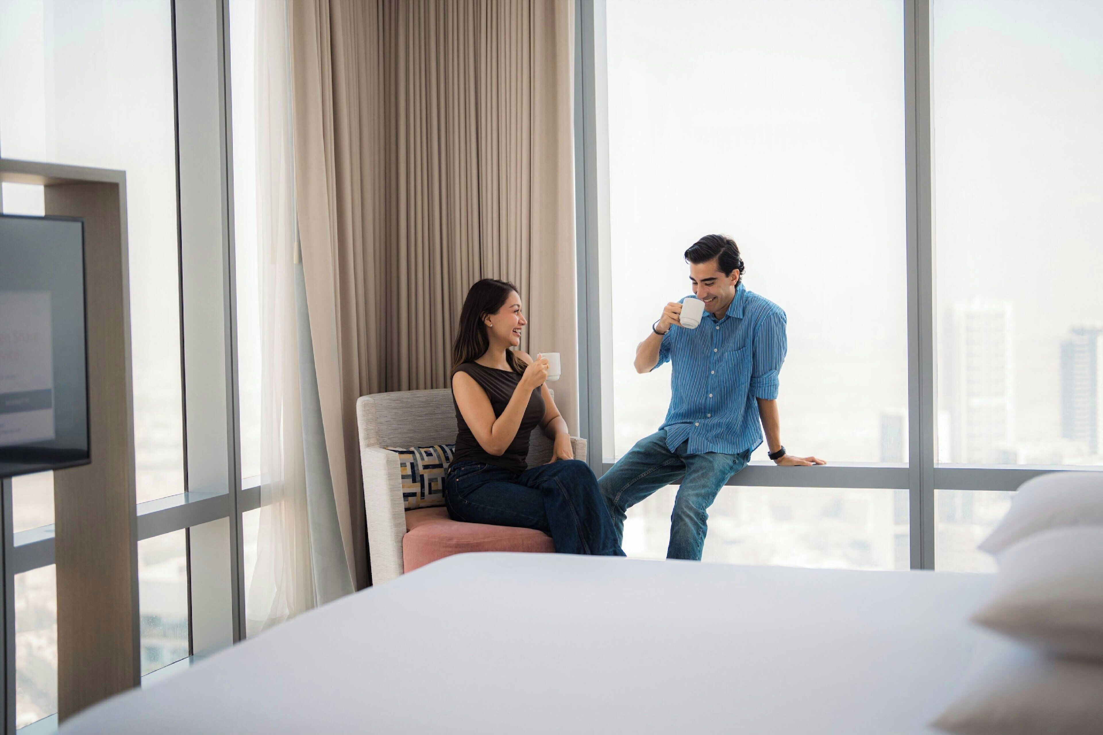 A modern hotel room with a large window, a bed, and a city view.