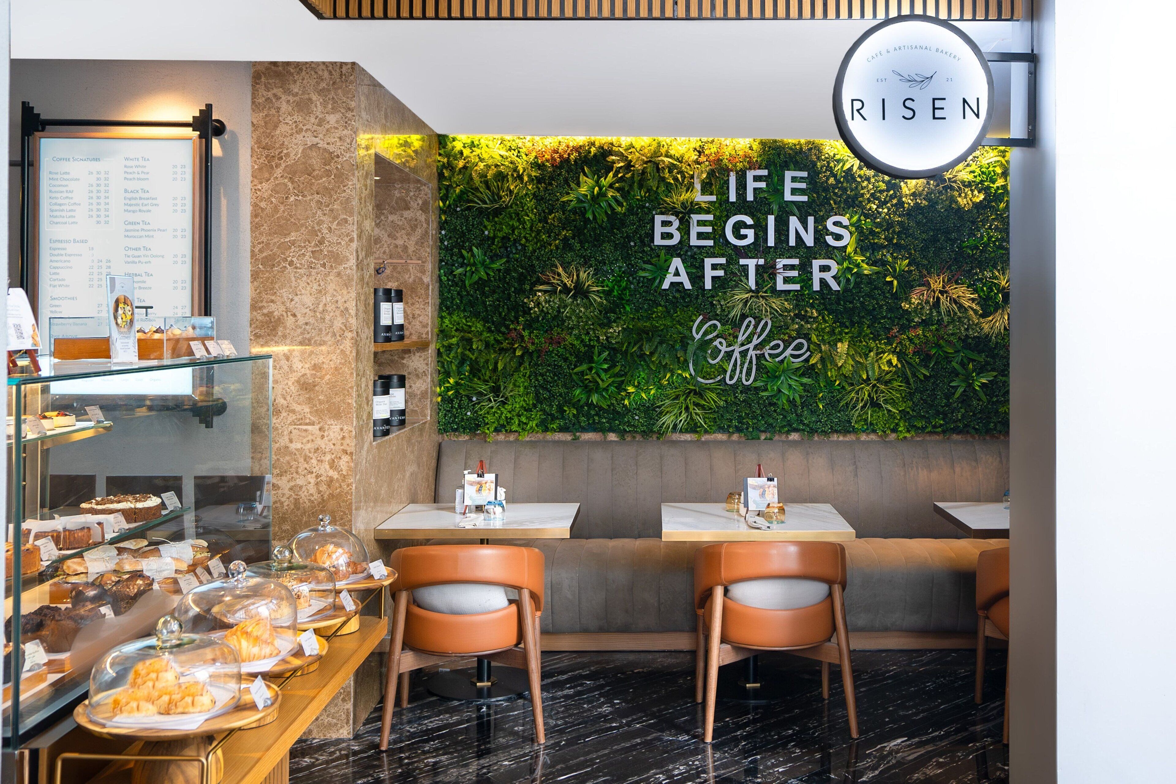A cafe interior with a menu board, a wall with greenery, and seating areas.