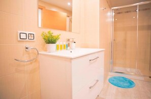 Bathroom features a white vanity, glass shower enclosure, and a potted plant.