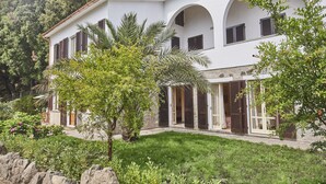 A white villa with arched windows and a stone facade, surrounded by lush greenery and a stone wall. - Marciana Hills Apartments (Marciana)