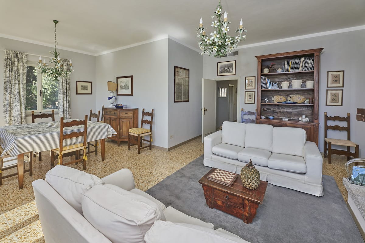 A living room with a white sofa, a wooden coffee table, a chandelier, and a bookshelf.
