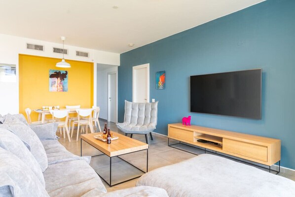 A modern living room with a sofa, a coffee table, a TV, and a dining area with chairs and a table.