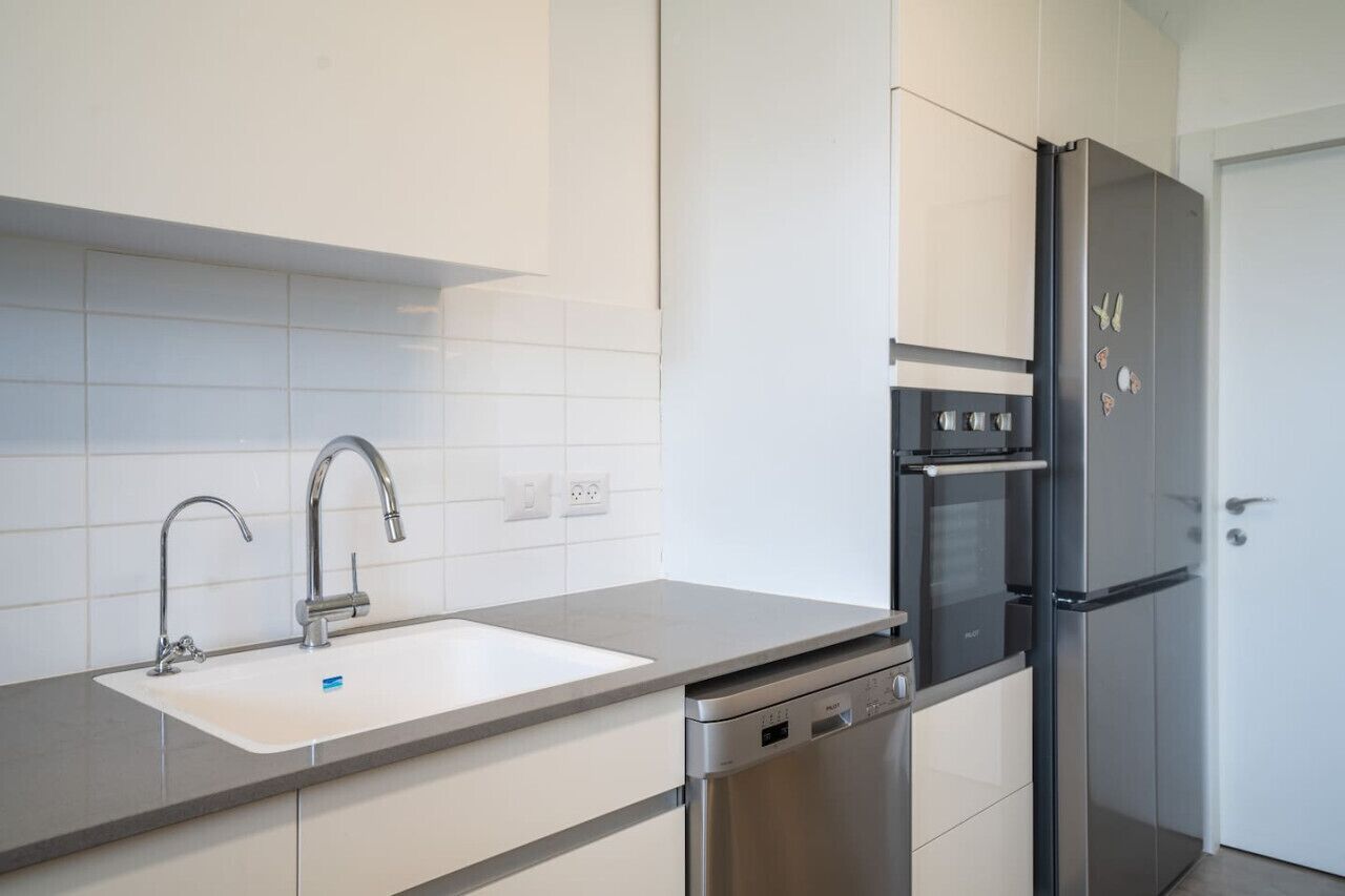 A modern kitchen with a stainless steel refrigerator, oven, dishwasher, and a white sink with a grey countertop.