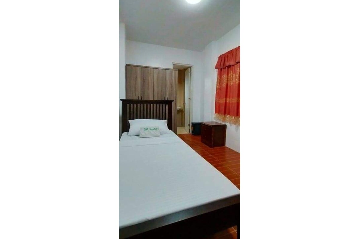 Ein Schlafzimmer mit einem Bett, einem Holzkopfende, einem roten Vorhang und einer kleinen Holzkiste.