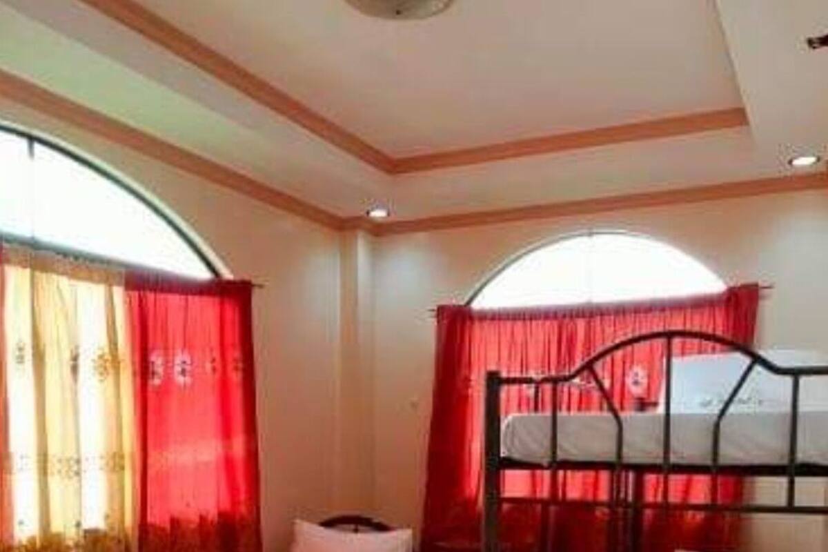 Une chambre de dortoir avec deux lits superposés, une fenêtre avec des rideaux rouges et un sol carrelé.