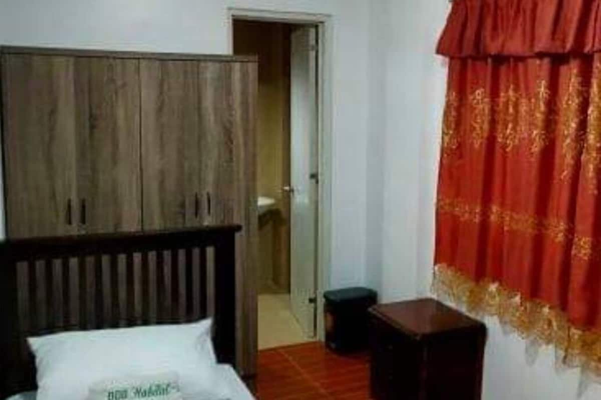 Une chambre à coucher avec un lit, une armoire en bois, un rideau rouge et une petite table.