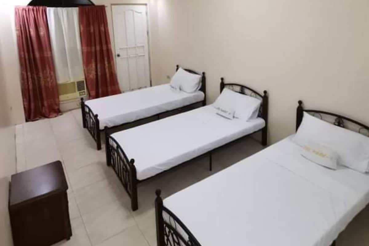 Une chambre avec trois lits simples, une petite table et une porte.