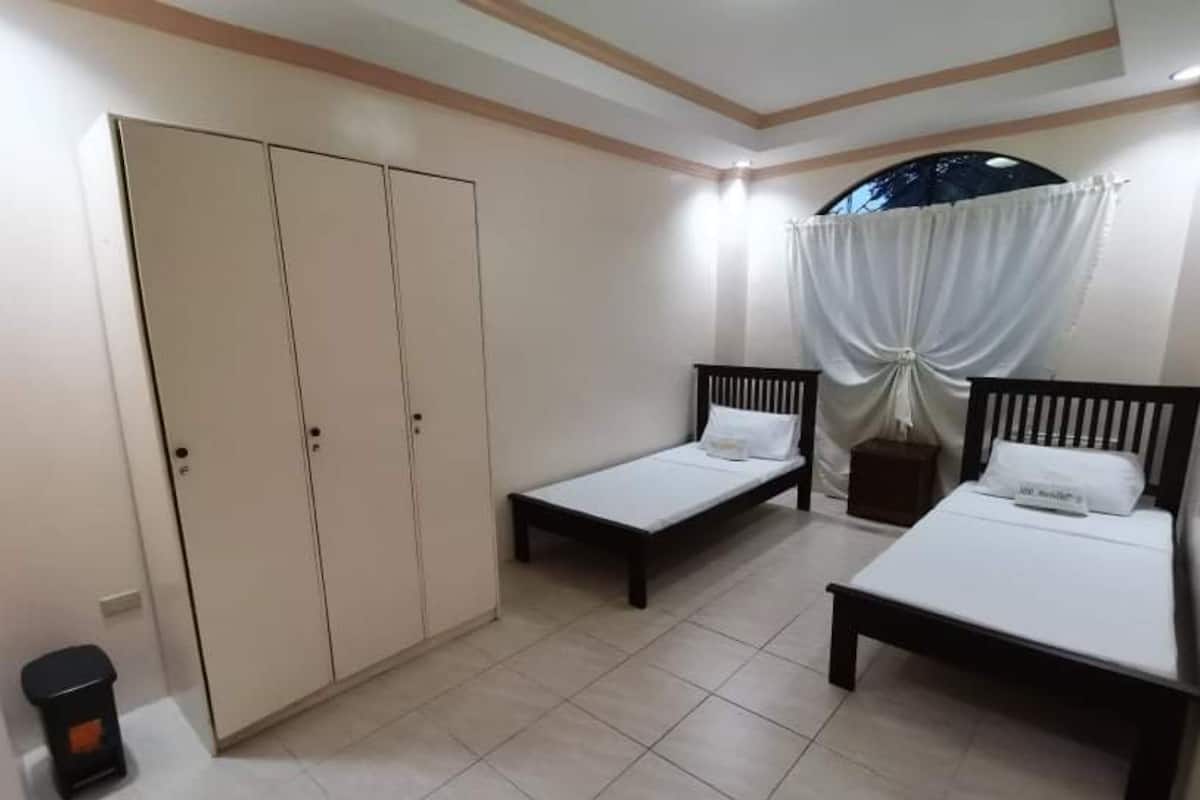 Une chambre avec deux lits simples, une armoire et une petite poubelle.