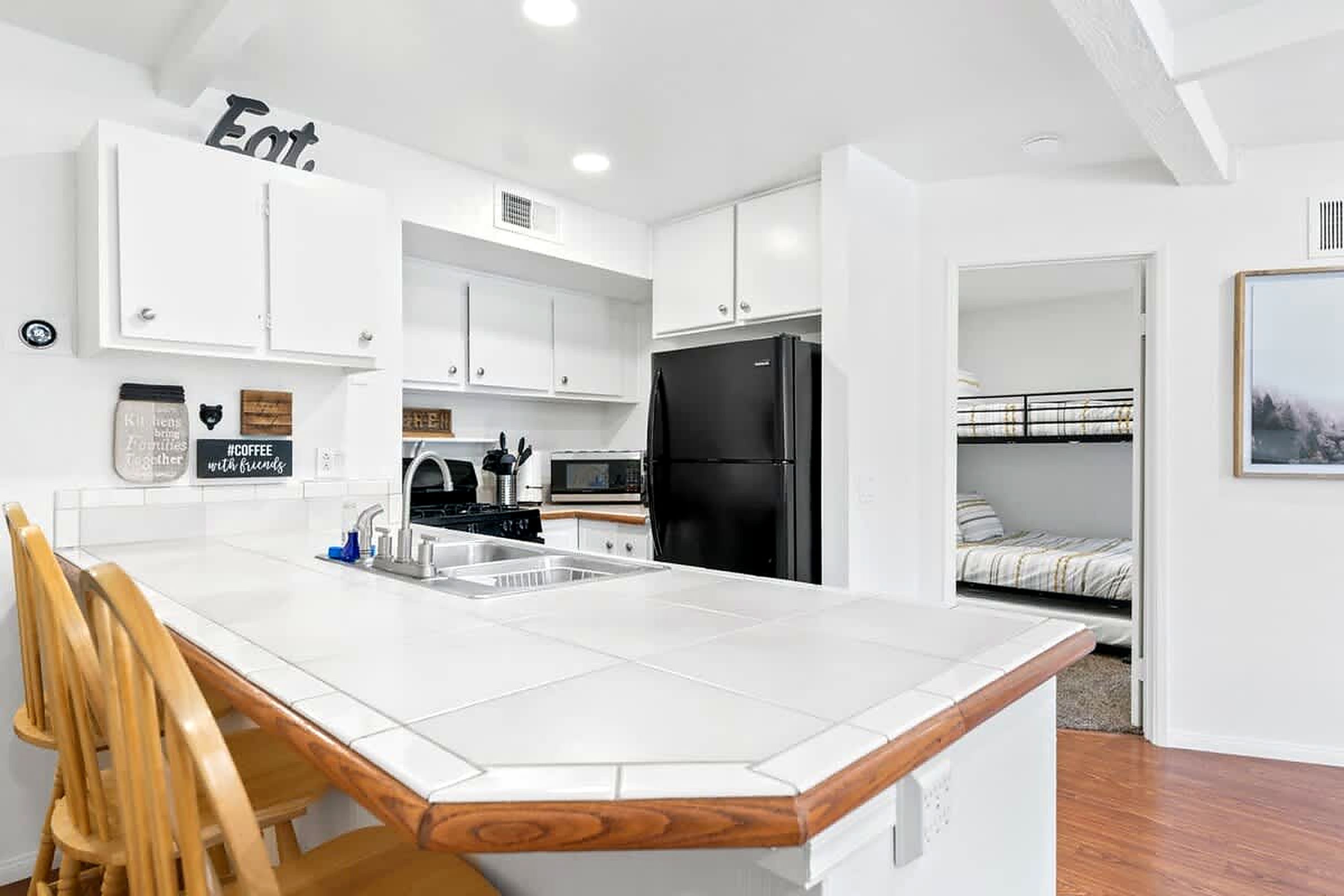 A compact kitchen with white cabinets, a black refrigerator, and a wooden chair.