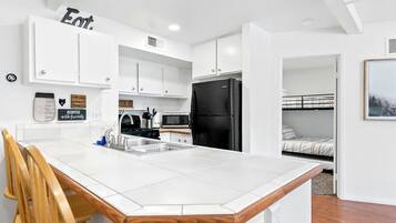 A compact kitchen with white cabinets, a black refrigerator, and a wooden chair.