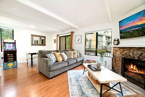 Ein modernes Wohnzimmer mit einem grauen Sofa, einem Kamin und Blick ins Freie durch große Fenster.
