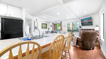 A modern kitchen with a black refrigerator, wooden chairs, a dining table, and a large window.