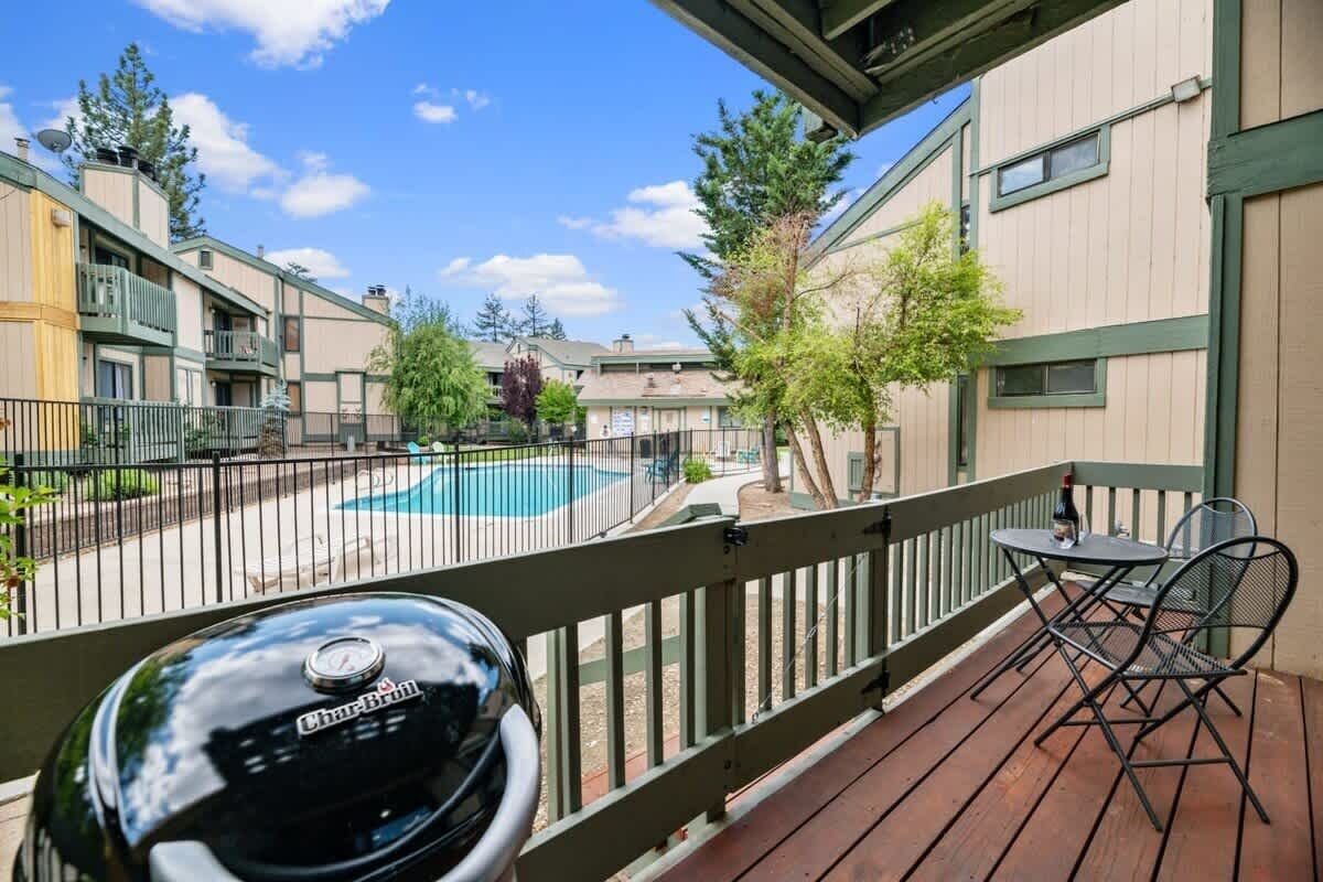 A balcony with a grill, a pool, and a view of apartment buildings.
