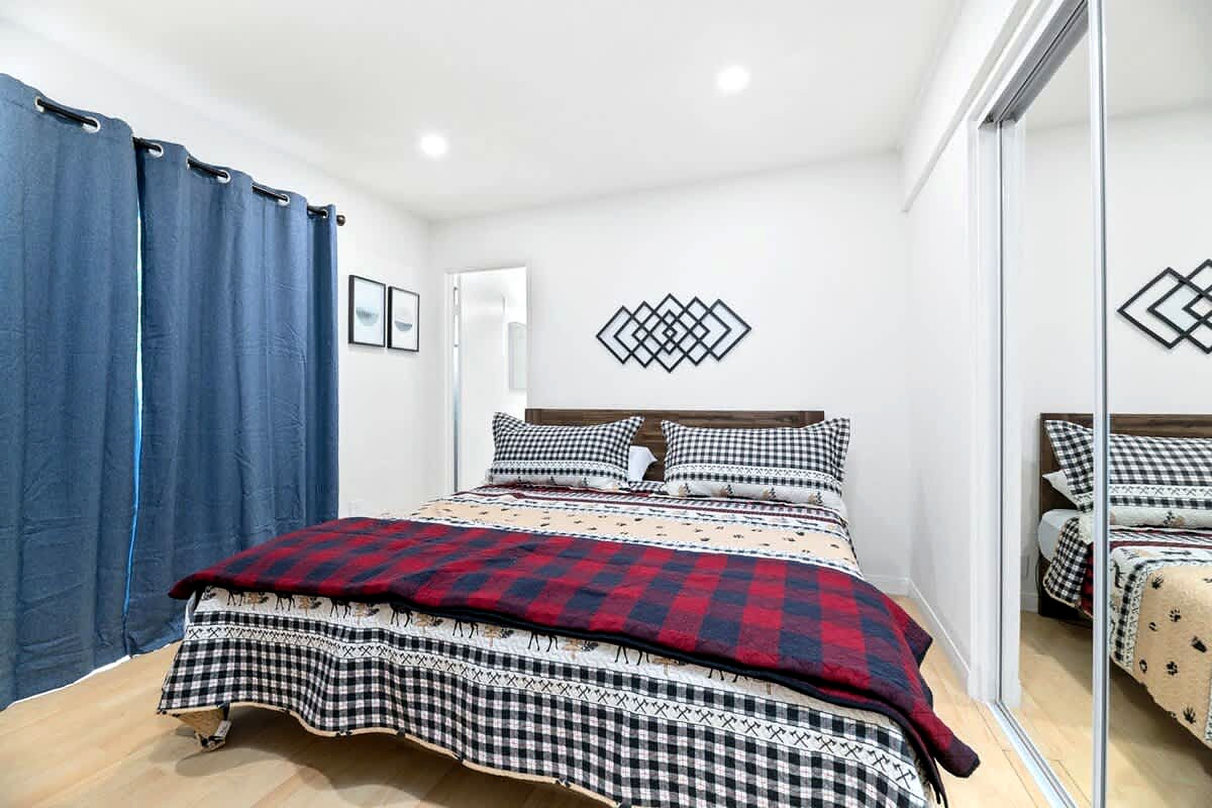 Une chambre à coucher avec un lit, une literie à carreaux, un rideau bleu et une décoration murale géométrique.
