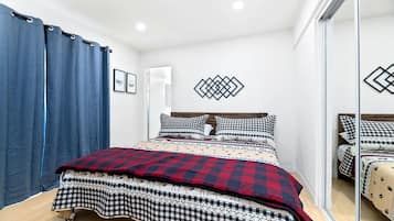 A bedroom with a bed, checkered bedding, a blue curtain, and a geometric wall decoration.