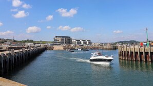 A marina with boats, a pier, and a modern building in the background. - West Bay Holiday Home (Bridport)
