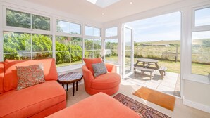 A sunlit room with a large glass door leading to an outdoor patio area. - West Bay Holiday Home (Bridport)