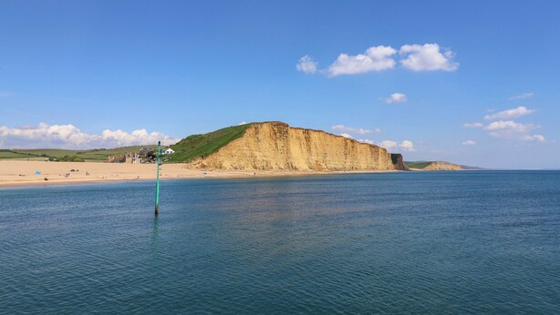 A coastal landscape with a sandy beach, a cliff, and a calm sea. - West Bay Holiday Home (Bridport)