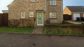 A two-story stone house with a green front door, multiple windows, and a visible garage. - West Bay Holiday Home (Bridport)