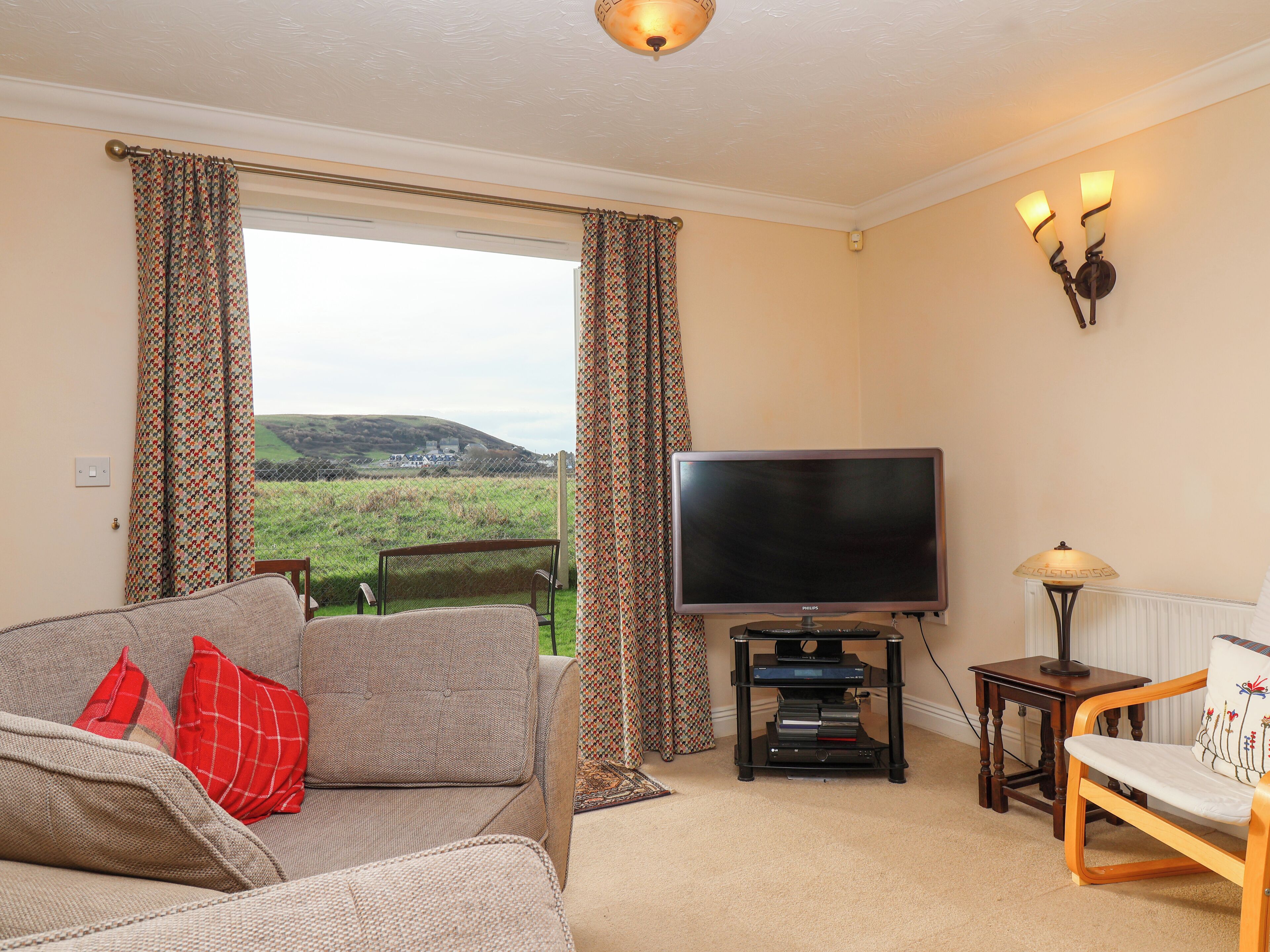 A living room with a sofa, a television, and a view of a green landscape through a window.