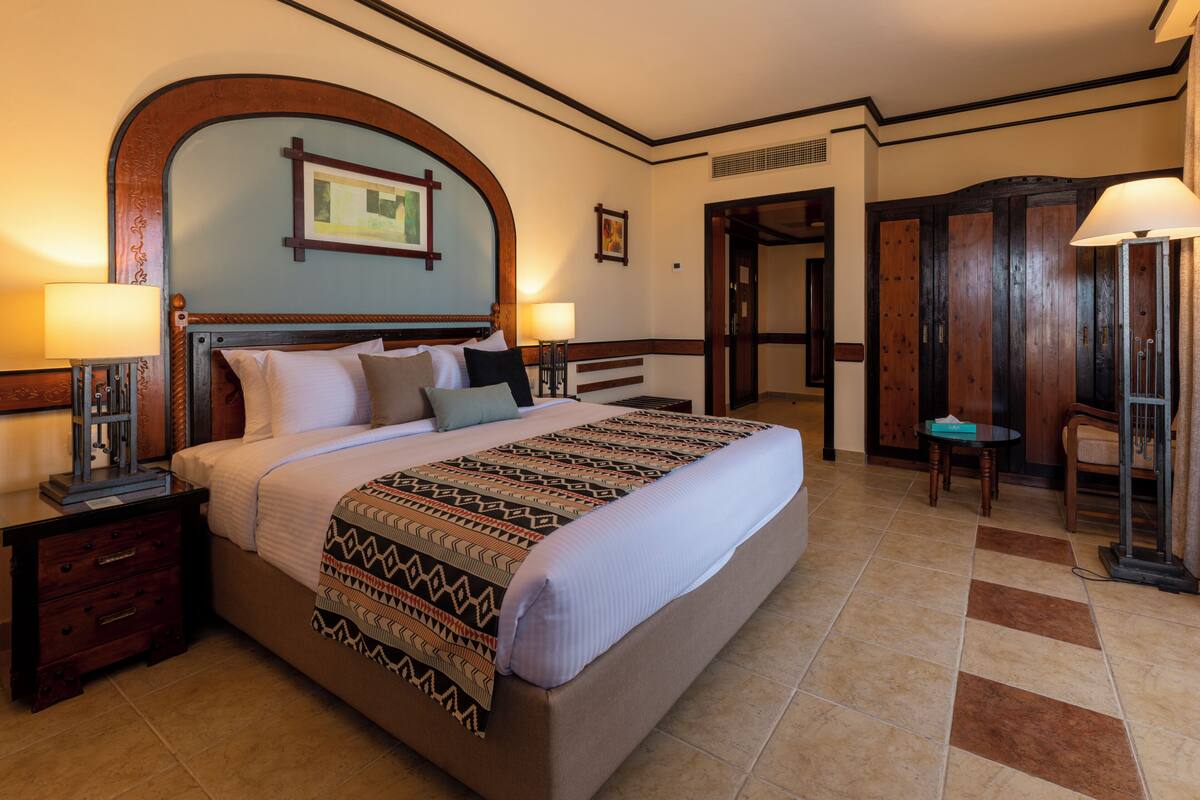 A neatly made bed with a patterned bedspread, two bedside tables with lamps, a wooden headboard, and a framed picture on the wall.
