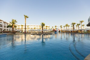 Una piscina amb palmeres i ombrel·les, envoltada d'edificis d'hotel.