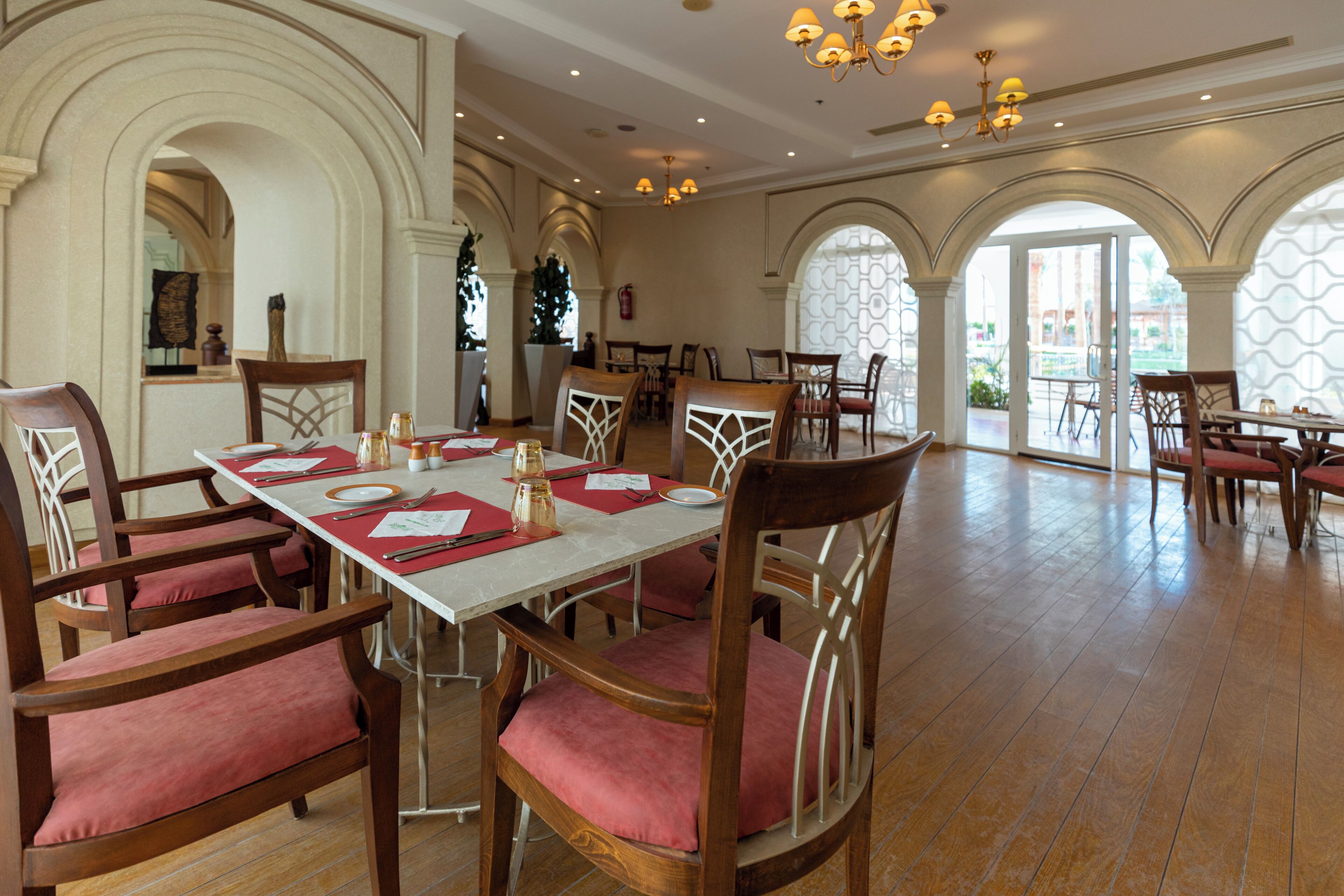 Un vaste espace dédié à la salle à manger, avec de nombreuses tables et chaises, de grandes fenêtres et un plafond haut orné de lustres.