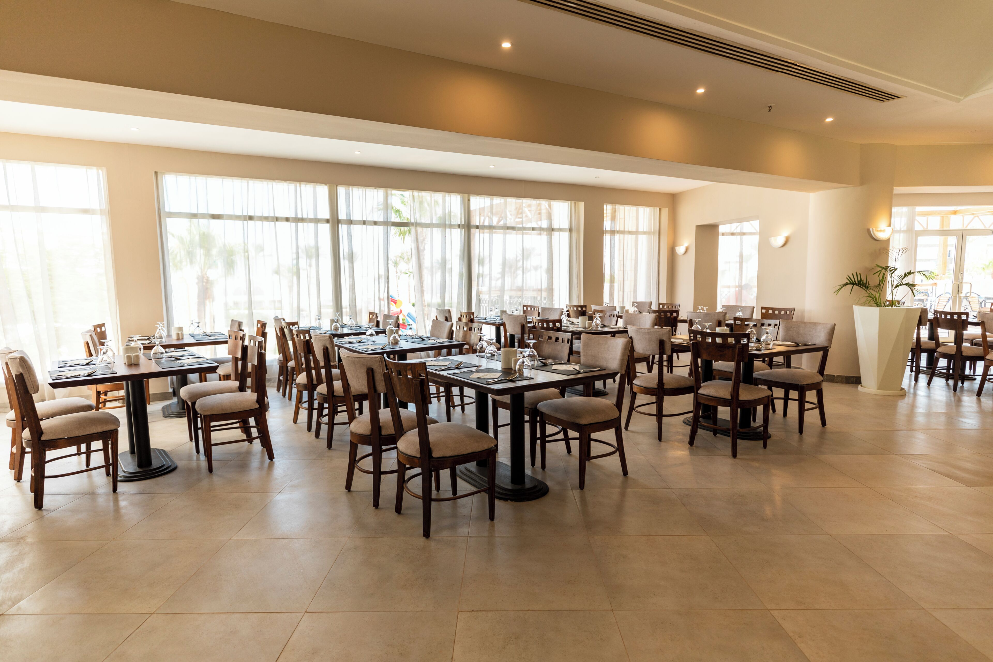 Un comedor amplio con varias mesas y sillas, ventanas grandes y un interior moderno y limpio.