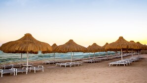 A beach with rows of sun loungers and thatched umbrellas.