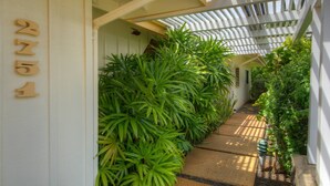 Un étroit sentier bordé d’une végétation luxuriante et un bâtiment blanc, sur lequel on peut voir le numéro « 2751 ».
