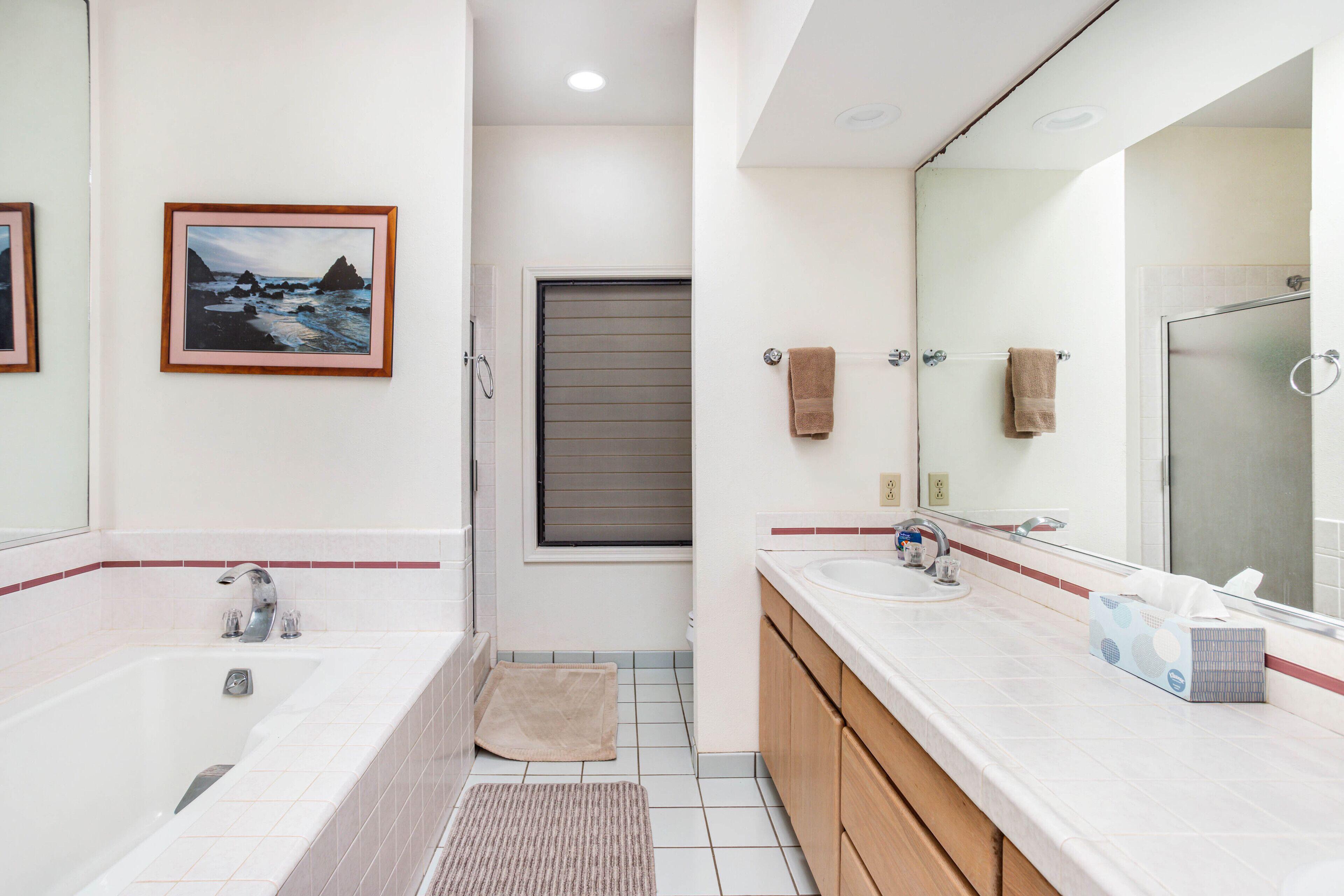 Ein modernes Badezimmer mit einer Badewanne, einem Waschbecken und einem großen Spiegel. An der Wand hängt ein gerahmtes Bild und eine Handtuchstange mit Handtüchern.