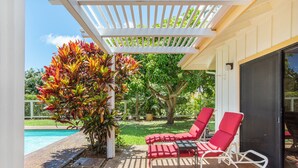 Un patio couvert avec deux chaises longues rouges, une piscine et une pergola ornée de plantes grimpantes.