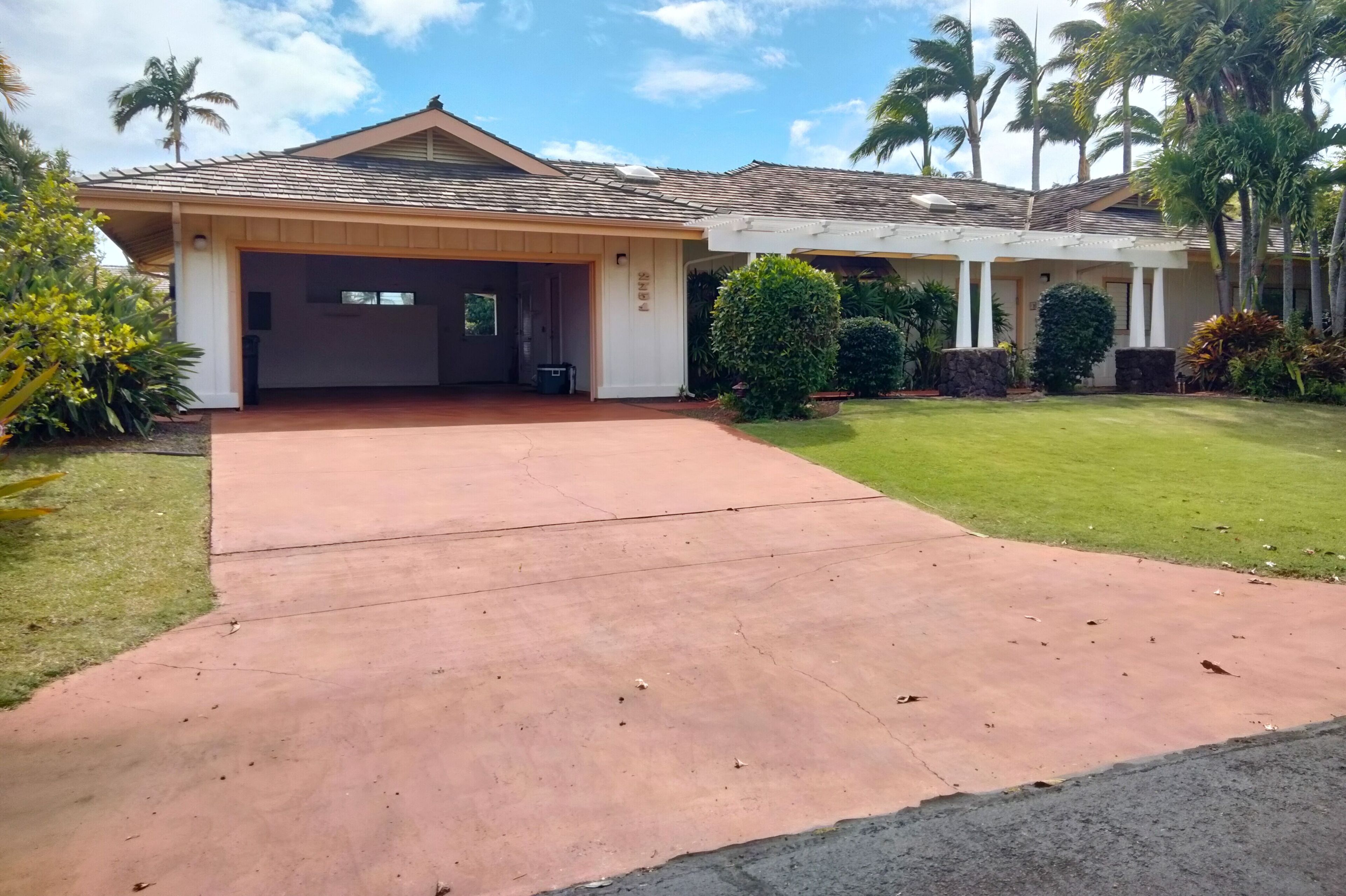 Uma casa residencial com garagem coberta, gramado bem cuidado e palmeiras ao fundo.