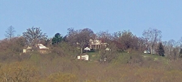 A hilltop view of a historic building with classical architecture, surrounded by trees and a clear sky.