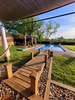 A wooden deck leading to a swimming pool with a pergola and outdoor seating area.
