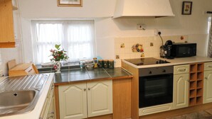 A kitchen with a sink, stove, microwave, and cabinets. There is a window with curtains and a vase with flowers on the counter.